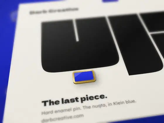 An enamel pin of the nuqta completing the word on its backing card